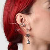 Woman wearing two silver wavy ear cuffs in narrow and wide with a silver dangle earring that features a coral shaped charm and a droplet charm