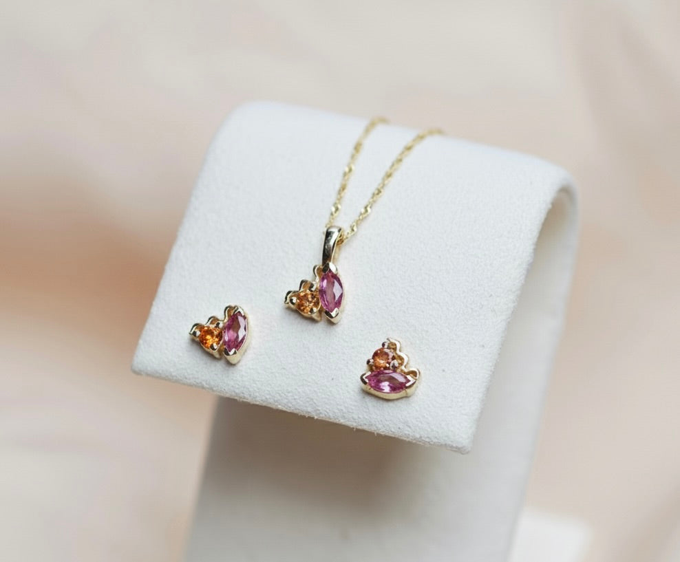 Gold jewelry set with pink and orange gemstones on a white stand against a beige background