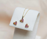 Gold jewelry set with pink and orange gemstones on a white stand against a beige background